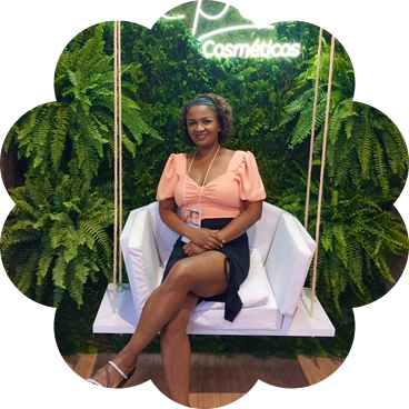 Jucelia Pereira, ex-técnica de enfermagem que transformou sua vida ao fundar uma loja de cosméticos, sentada em um balanço cercada por folhagens.
